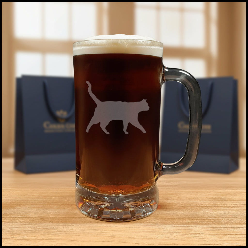 A clear glass beer mug filled with dark beer and topped with white foam, featuring a cat silhouette etched on the front.