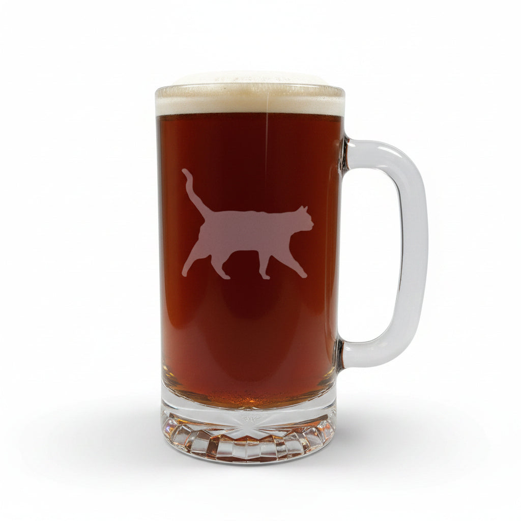 A clear glass beer mug filled with dark beer and topped with white foam, featuring a cat silhouette etched on the front, set on a light wood surface against a white background.