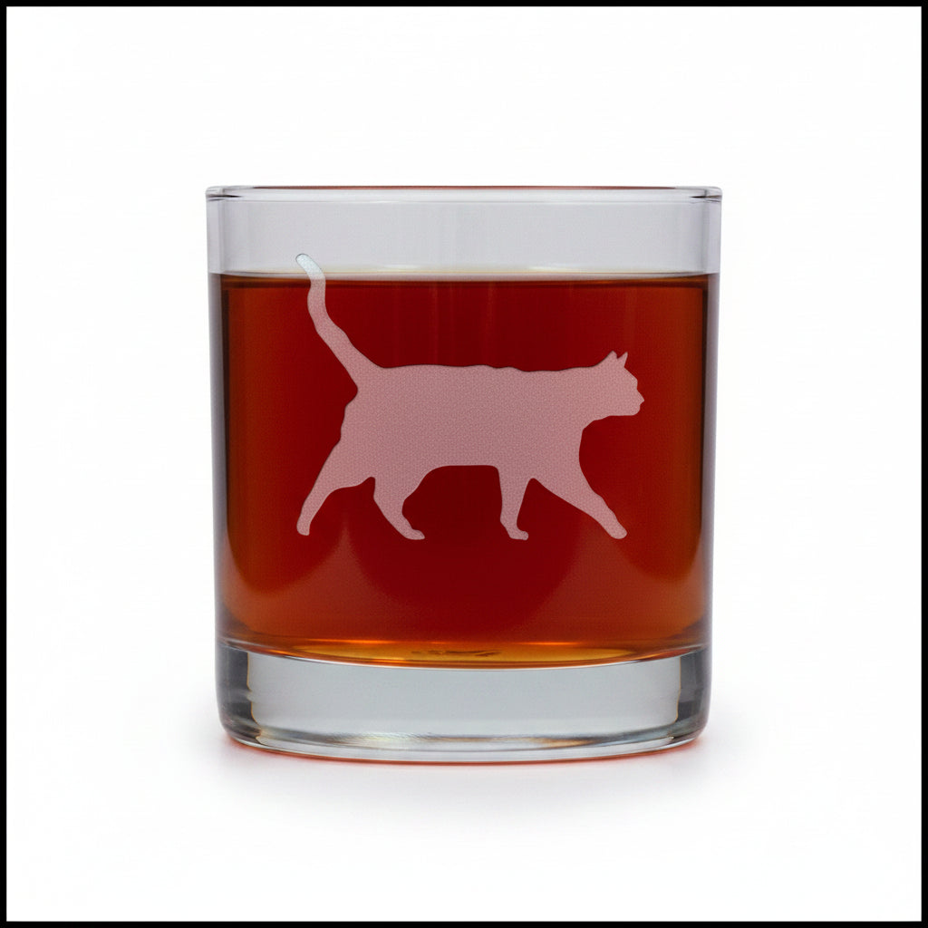 A clear rocks glass filled with an amber-red liquid, featuring a etched cat silhouette design on the front, set against a white background.