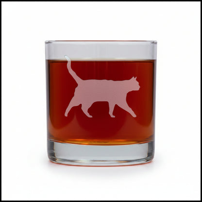 A clear rocks glass filled with an amber-red liquid, featuring a etched cat silhouette design on the front, set against a white background.