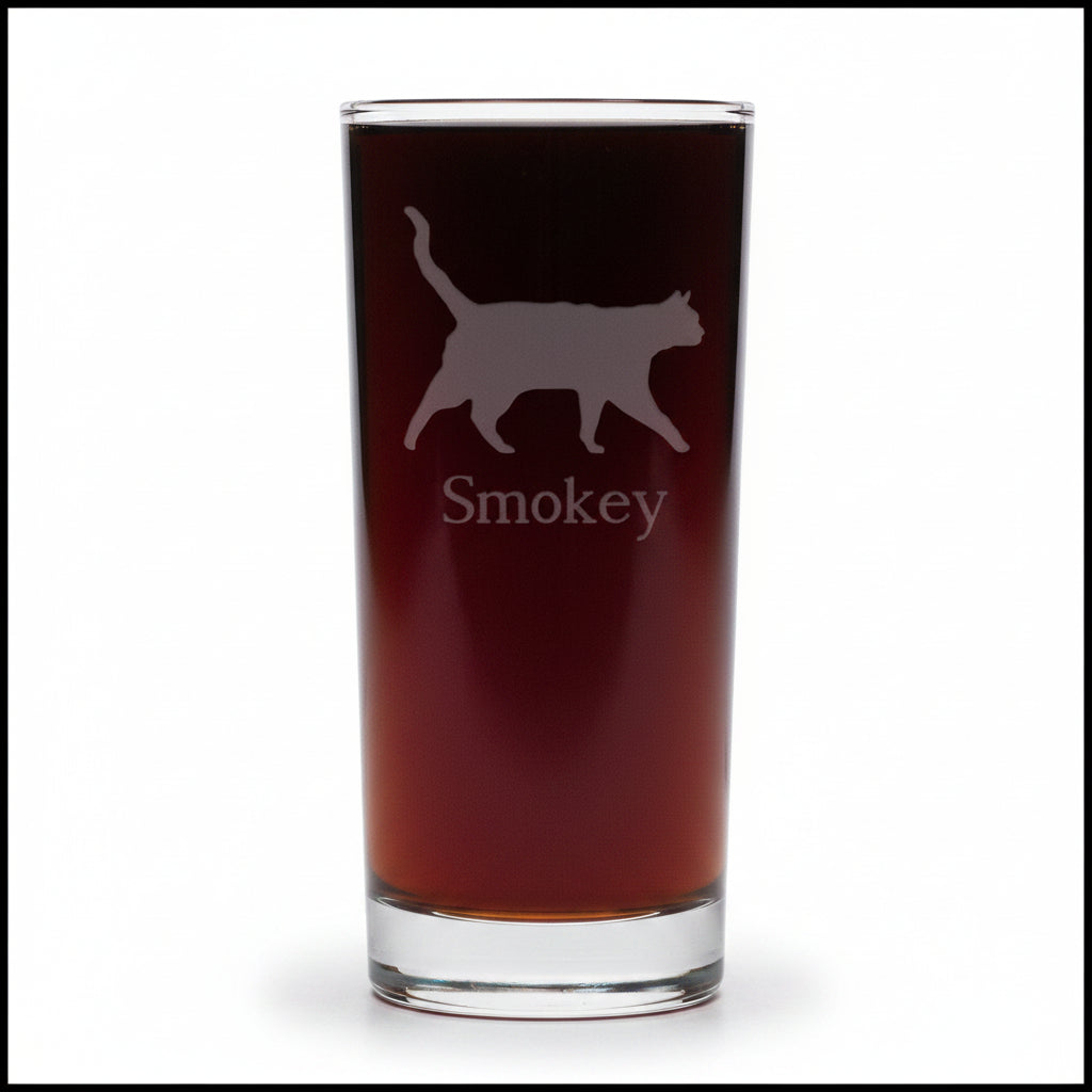 A clear pint glass filled with dark beer, featuring an etched silhouette of a cat and the name 'Smokey' on the front, set against a white background.