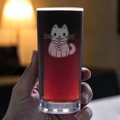 A hand holds a clear glass cooler glass filled with a dark red beverage. The glass features an etched cute cat wearing a collar.