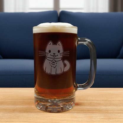 A clear glass beer mug filled with dark beer and topped with white foam, featuring an etched cute cat design on the front, set on a wooden surface against a blue couch in the background.