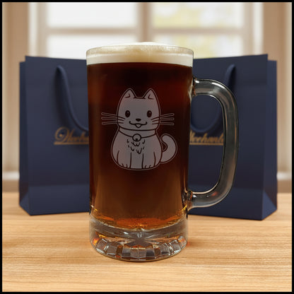 A clear glass beer mug filled with dark beer and topped with white foam, featuring an etched cute cat illustration on the front, set on a wooden surface against a black background.
