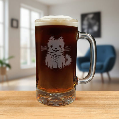 A clear glass beer mug filled with dark beer and topped with white foam, featuring an etched cute cat design on the front, set on a wooden surface against a living room background.