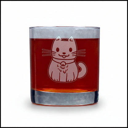 A clear glass rocks tumbler filled with a dark red liquid, featuring an etched design of a cat wearing a collar on the front. The tumbler is set on a light gray wooden surface against a white background.