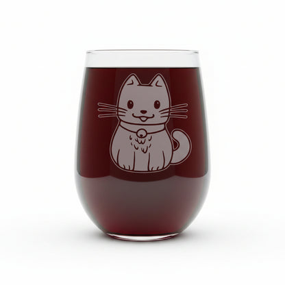 A clear stemless wine glass with an etched cute cat illustration on the front, set on a wooden surface against a solid white background.
