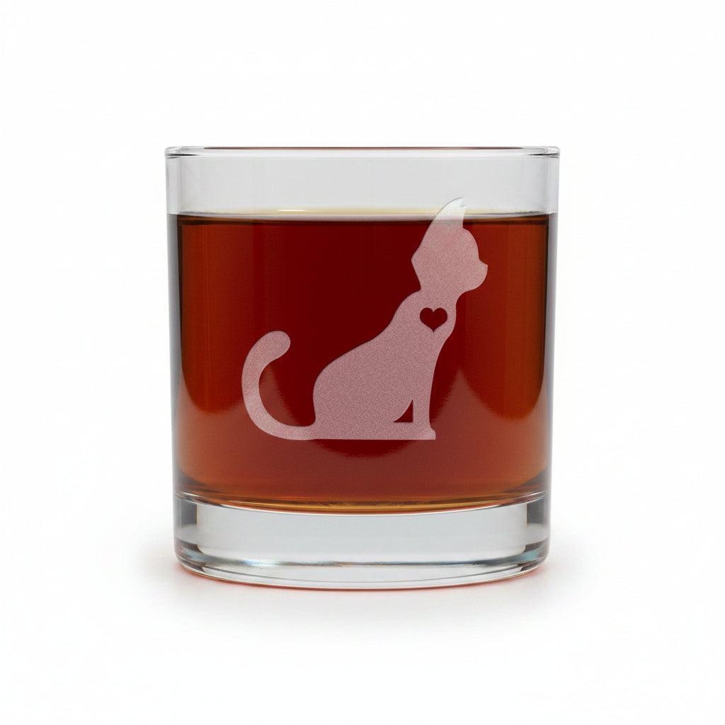 A clear glass rocks tumbler filled with amber-red liquid, featuring an etched cat silhouette with a small heart on the side, set against a white background.