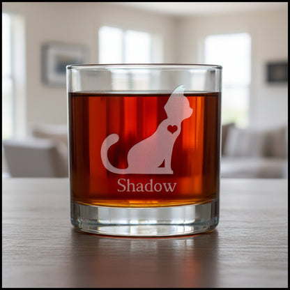 A clear glass rocks tumbler filled with a dark red drink, featuring an etched cat silhouette with a heart and the name 'Shadow' below it.