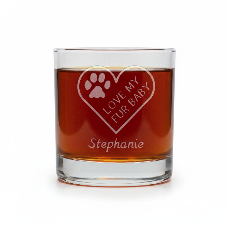 A clear glass rocks tumbler filled with amber liquid, featuring an etched heart design with a paw print and the words 'LOVE MY FUR BABY' along with the name 'Stephanie' below, set against a white background.