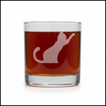 A clear rocks glass filled with dark red liquid, featuring a frosted white cat silhouette design on the front, set against awhite  background.