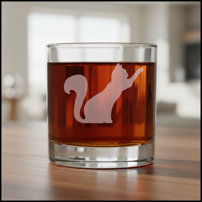 A clear rocks glass filled with amber-red liquid, featuring an etched silhouette of a playful on the front, set against a textured gray background.
