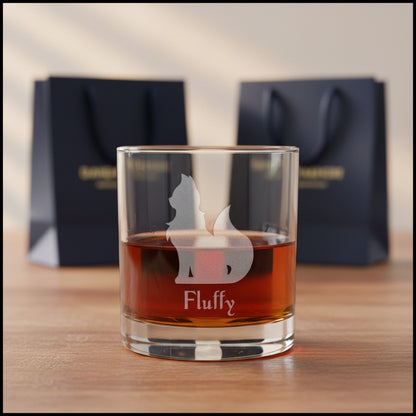 A clear rocks glass filled with an amber-red drink, featuring  an etched cat silhouette and the name 'Fluffy' printed below. 