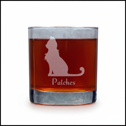 A clear rocks glass filled with an amber-red liquid, featuring a frosted pinkish cat silhouette and the name 'Patches' on the front, set against a white background.