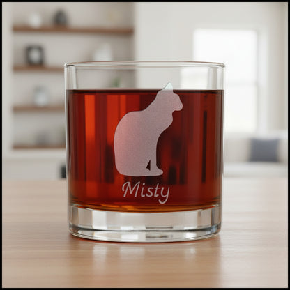 A clear glass rocks tumbler filled with an amber-red drink, featuring an etched cat silhouette and the name 'Misty' on the front.