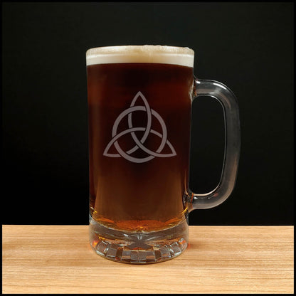 Glass mug with a Celtic knot design filled with dark beer on a wooden surface.