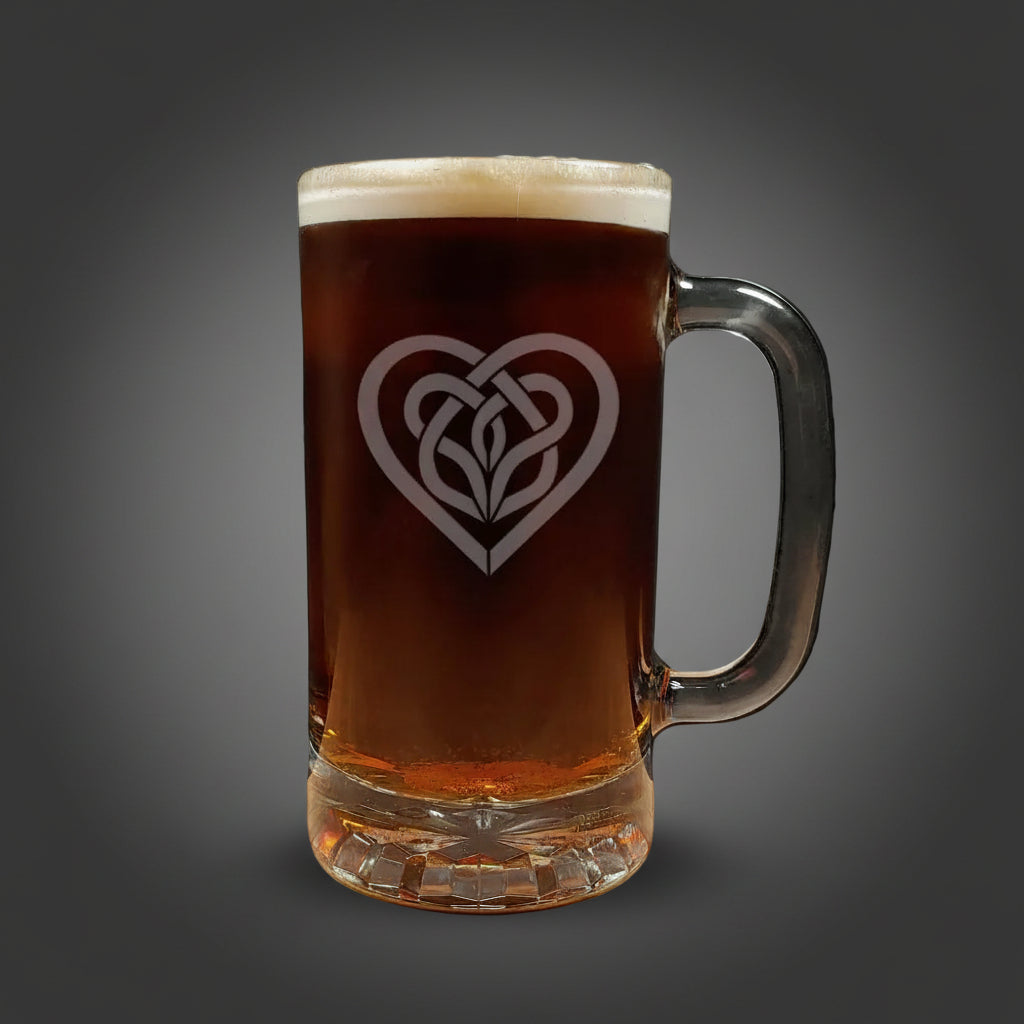 Glass mug with a heart-shaped Celtic knot design filled with dark beer on a wooden surface.
