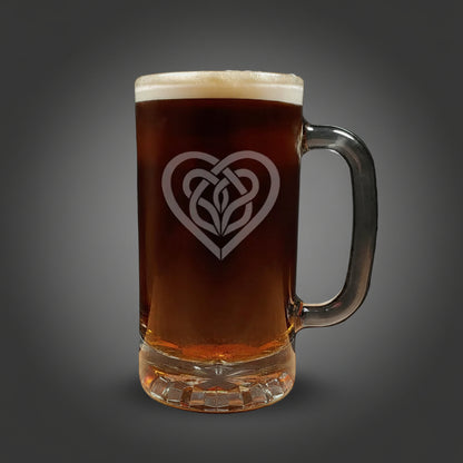Glass mug with a heart-shaped Celtic knot design filled with dark beer on a wooden surface.