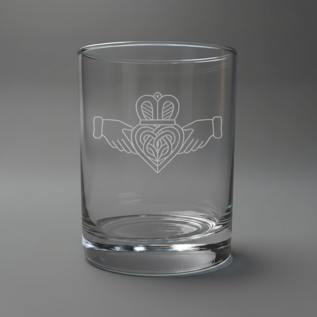 Etched Claddagh on a Clear whiskey glass with some whiskey in the glass, on a highlighted grey background. 