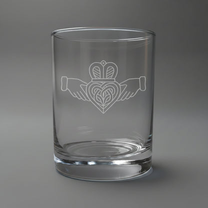 Etched Claddagh on a Clear whiskey glass with some whiskey in the glass, on a highlighted grey background. 