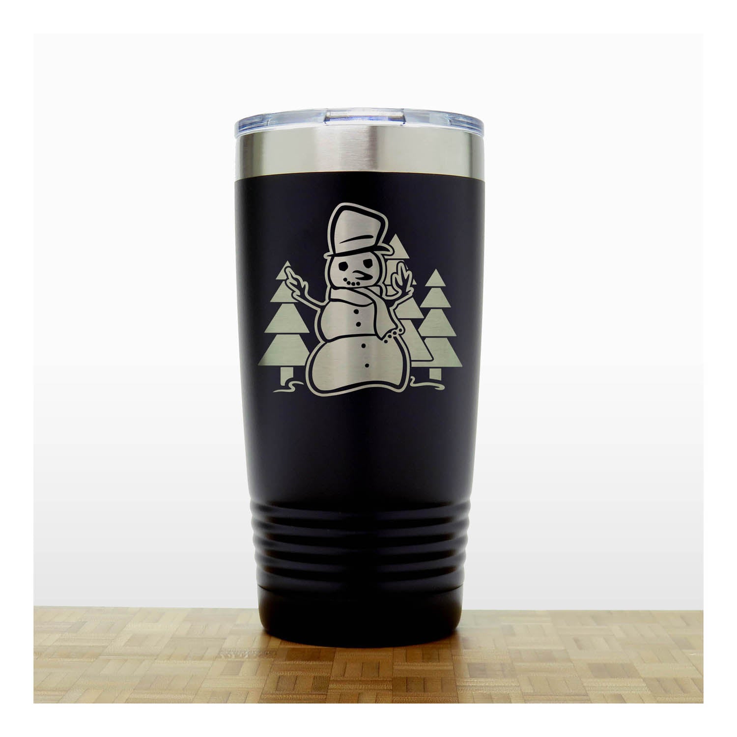 Black 20 oz Insulated Tumbler with the design of a snowman standing in front of Christmas trees - Copyright Hues in Glass