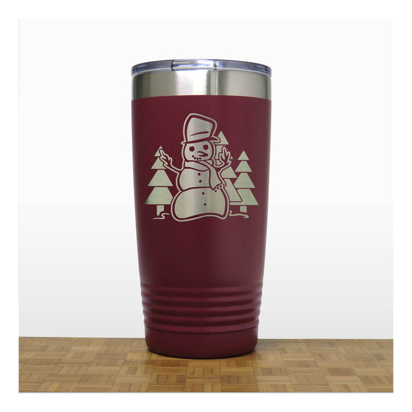 Maroon 20 oz Insulated Tumbler with the design of a snowman standing in front of Christmas trees - Copyright Hues in Glass