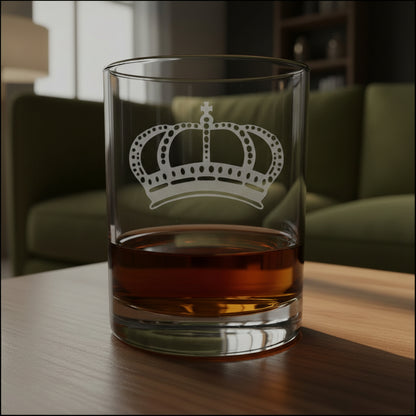 Clear whiskey glass with a permanent sand etched crown design, partially filled with whiskey on a wooden tabletop.