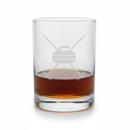 A clear glass rocks tumbler with an etched curlingdesign, partially filled with an amber-brown liquor, on a white background.