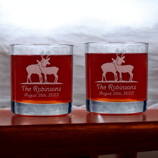 Two glasses with engraved stag and doe design and text on a wooden surface
