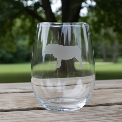 A clear stemless wine glass with a etched bulldog silhouette design  shown on a wooden surface with a tree in the background.