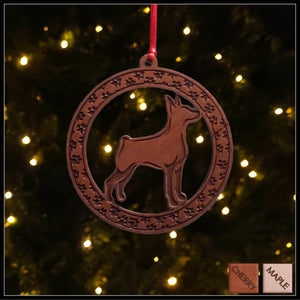 A round cherry wood veneer ornament with a border of small paw prints. The center of the ornament is a Doberman dog.