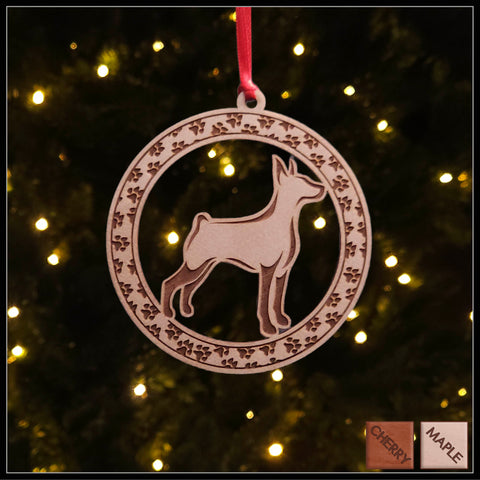 A round maple wood veneer ornament with a border of small paw prints. The center of the ornament is a Doberman dog.