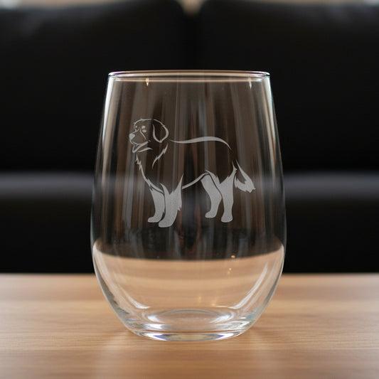 Clear glass with astemless wine glass with a  bernese mountain  dog etching on a wooden surface and black couch  in the background