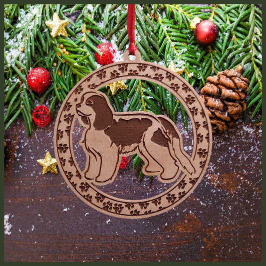 A round maple wood veneer ornament with a border of small paw prints. The center of the ornament is a Cavalier King Charles dog.