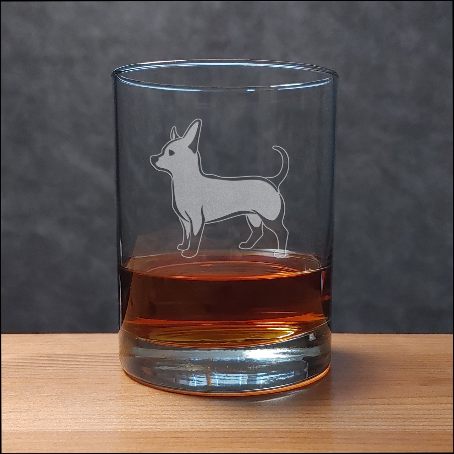 Clear glass tumbler with a dog engraving filled with amber liquid on a wooden surface.