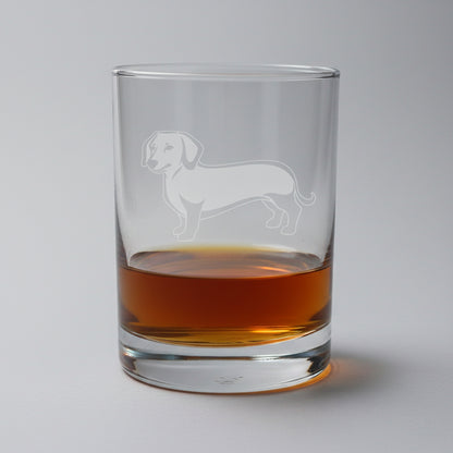 Clear glass with dachshund engraving containing a amber liquor on a on a softly lite background