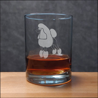 Clear glass with a poodle dog engraving filled with amber liquid on a wooden surface.