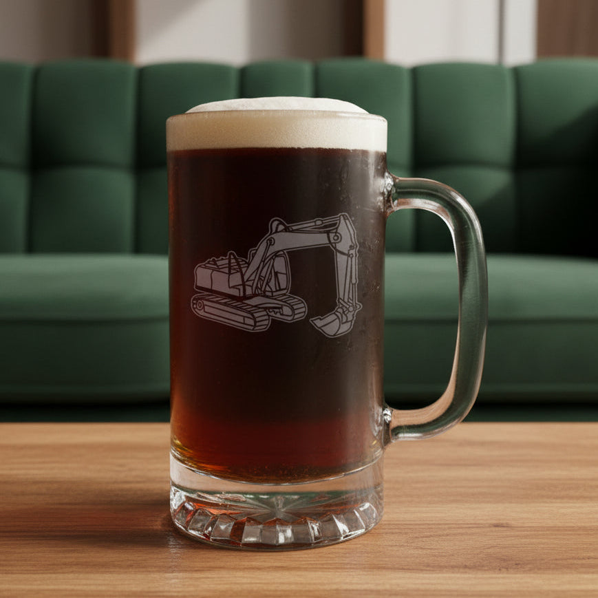 A clear glass beer stein mug with a handle, filled with dark brown beer and topped with white foam, featuring an etched excavator design. The mug sits on a wooden surface against a green couch