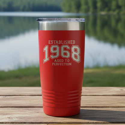 Red tumbler with silver rim and text 'Established 1968 Aged to Perfection' with a still lake in the  background