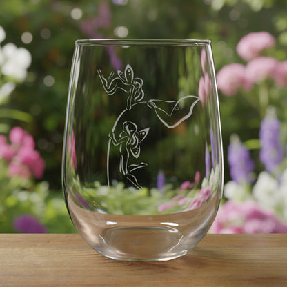 Clear glass with etched design of  fairies hovering on the stem of a lily flower on a wooden surface and a garden in the background