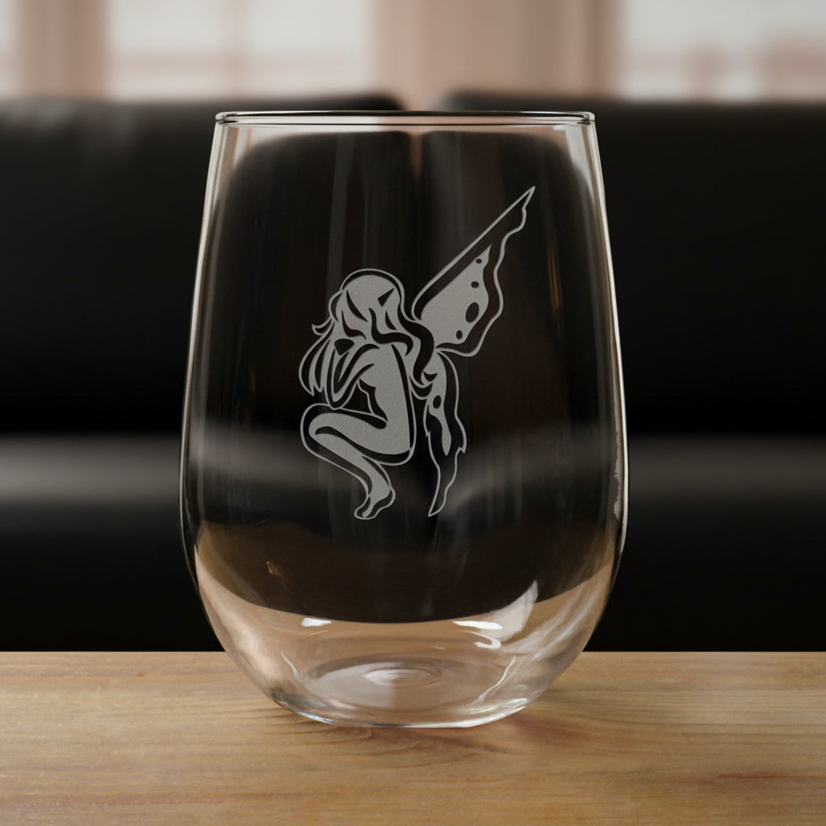 Clear glass with a etched  design of a fairy on a wooden surface and black couch in the background