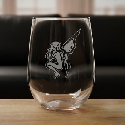 Clear glass with a etched  design of a fairy on a wooden surface and black couch in the background