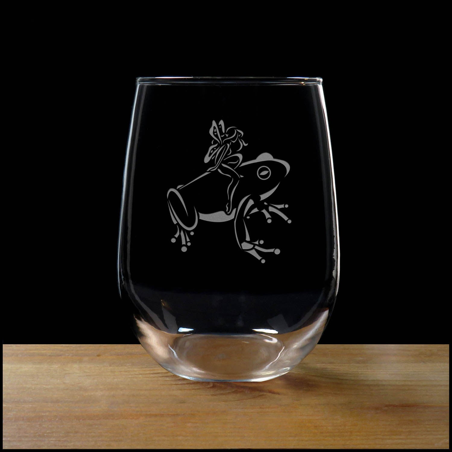 17oz Stemless Wine Glass with an etched image of a frog, on a wood surface and a black background
