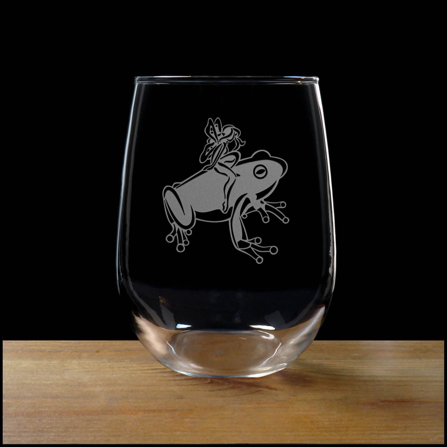 17oz Stemless Wine Glass with an etched image of a frog, on a wood surface and a black background