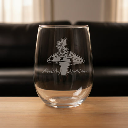 Clear glass with a engraved design of a fairy on a toadstool on a wooden surface with a black couch in the  background