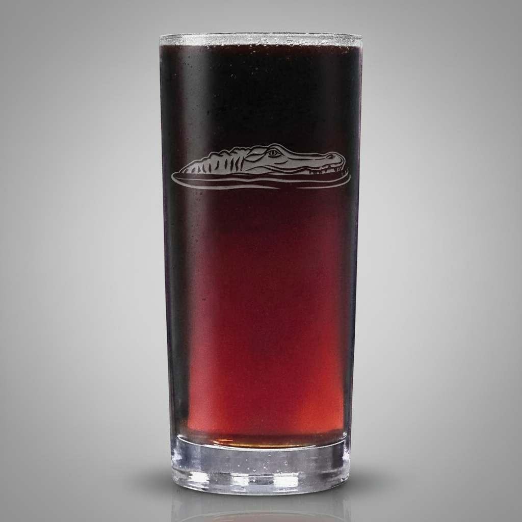 A tall, slender clear glass tumbler filled with a dark red liquid, featuring an  etched alligator design on the front, isolated on a light grey background.