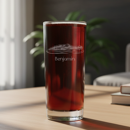 A clear cooler with a handle, filled with dark amber beer and topped with white foam, featuring a white crown design  on the front, set on a light wood surface with a living room  background. 