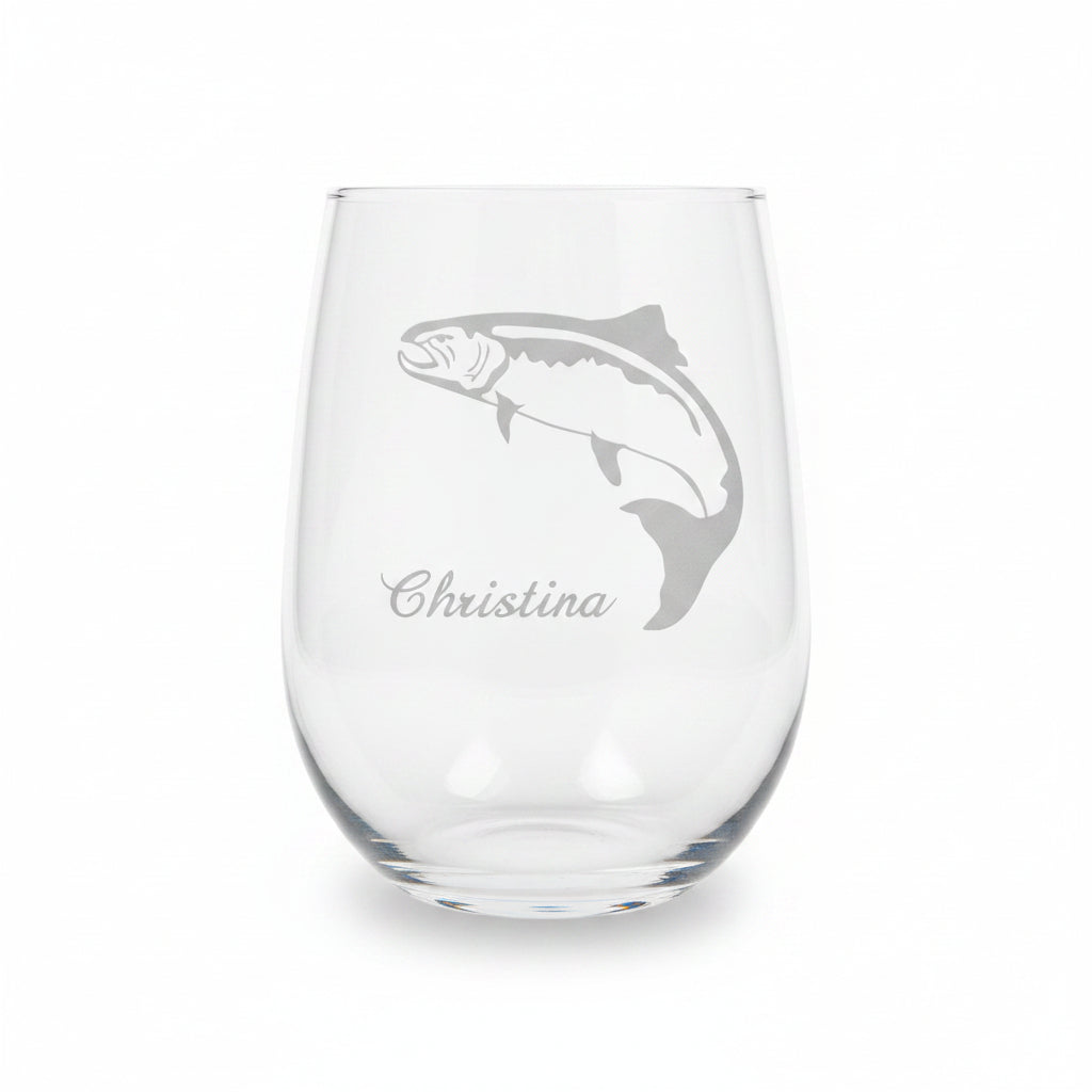 A clear stemless wine glass with an etched fish silhouette and the name 'Christina' on the front, displayed on a wooden surface against a solid white background.