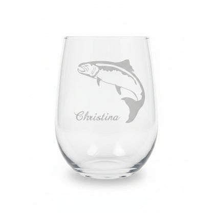 A clear stemless wine glass with an etched fish silhouette and the name 'Christina' on the front, displayed on a wooden surface against a solid white background.