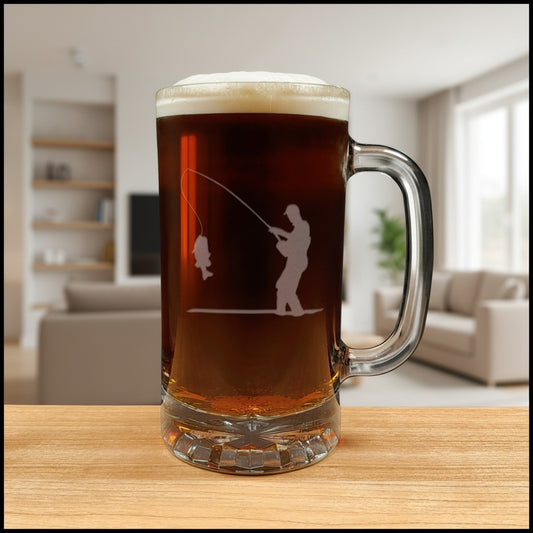 A frosted glass beer mug with a handle, filled with dark beer and topped with white foam, featuring an etched fishing silhouette on the front, set on a wooden table with a blurred living room background.
